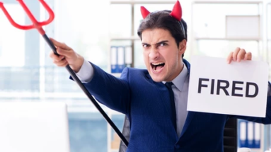A man in a suit with halloween demon horns and pitchfork, holding a sign that says "FIRED"