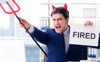 A man in a suit with halloween demon horns and pitchfork, holding a sign that says "FIRED"